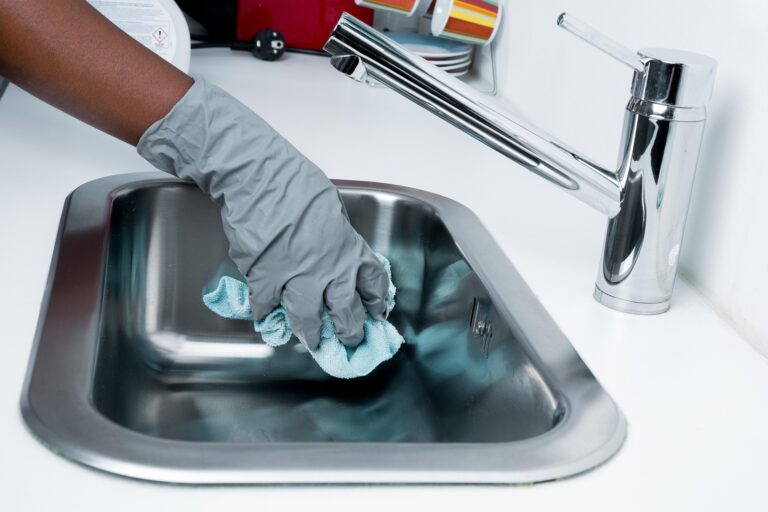Hay una mano con guantes limpiando un lavaplatos